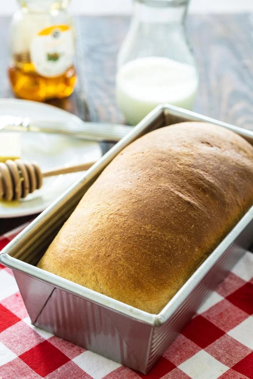 Loaf of Buttermilk Bread in a loaf pan with honey and buttermilk in background.