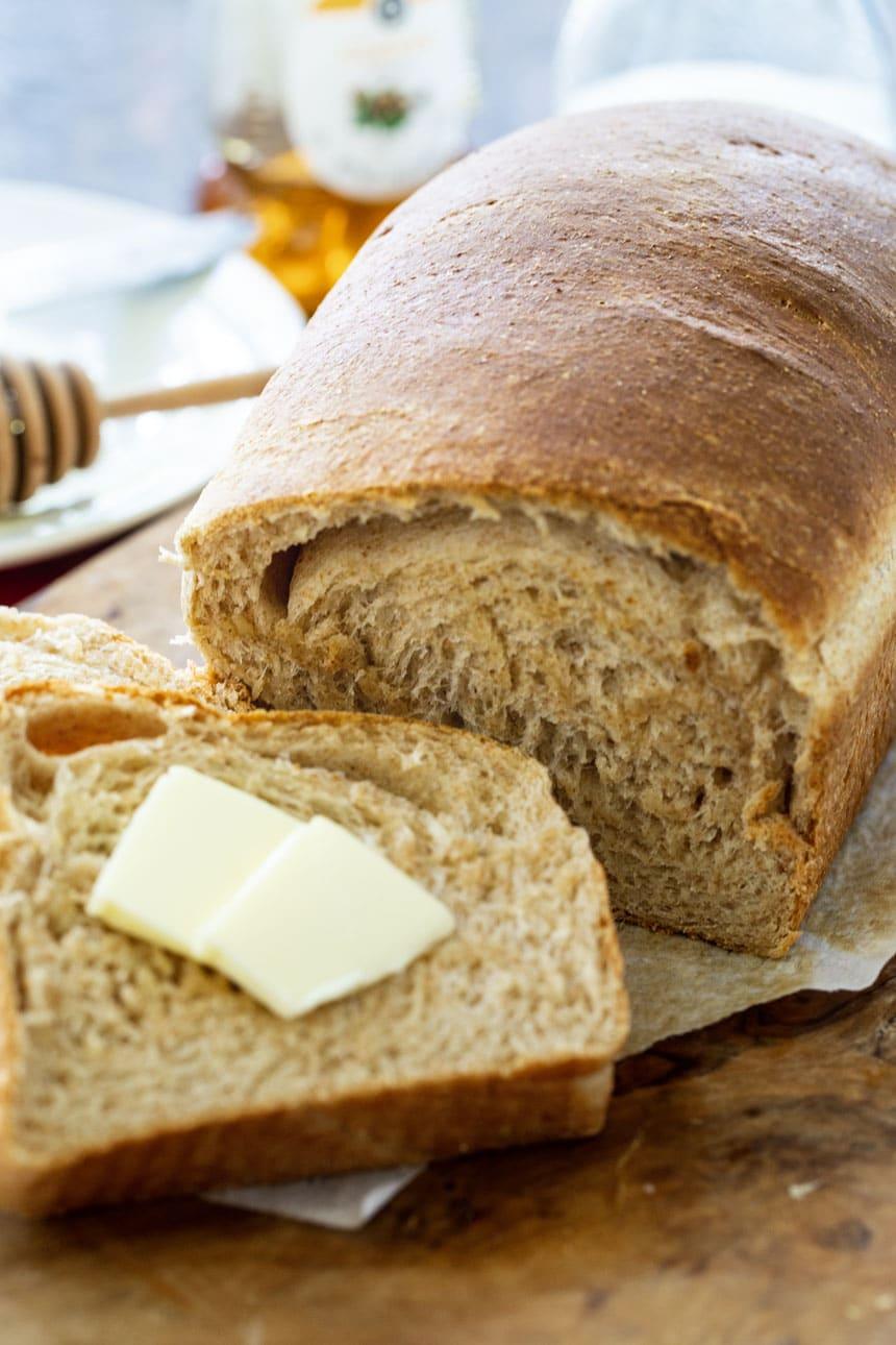 Slice of bread topped with butter next to the rest of the loaf.