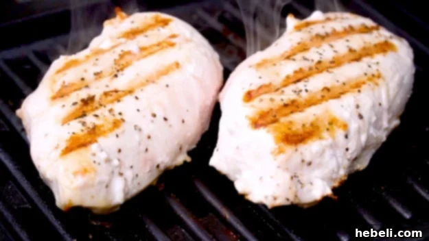 Two perfectly grilled chicken breasts on a cutting board.