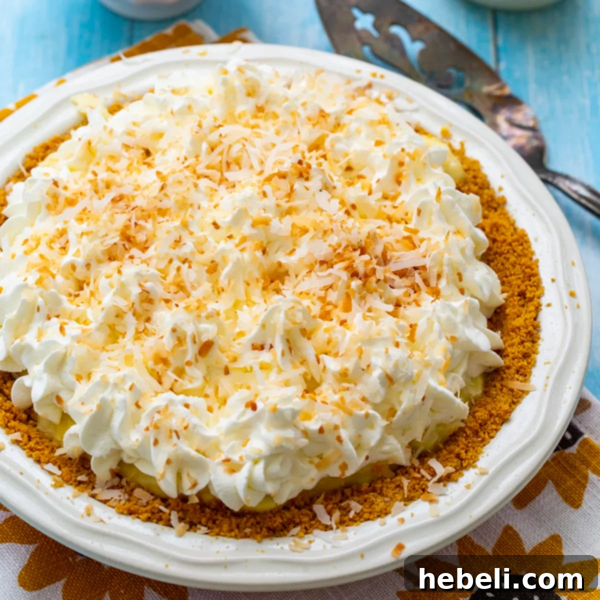 Whole coconut cream pie in a pie pan, adorned with toasted coconut and whipped cream.