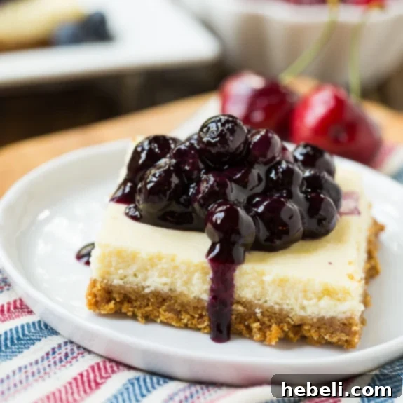 Creamy Lightened-Up Cheesecake Bars on a graham cracker crust, topped generously with fresh blueberries and cherries.