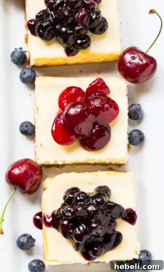 A beautifully arranged plate of five Lightened-Up Cheesecake Bars, some adorned with blueberry topping and others with cherry topping, showcasing their inviting presentation.