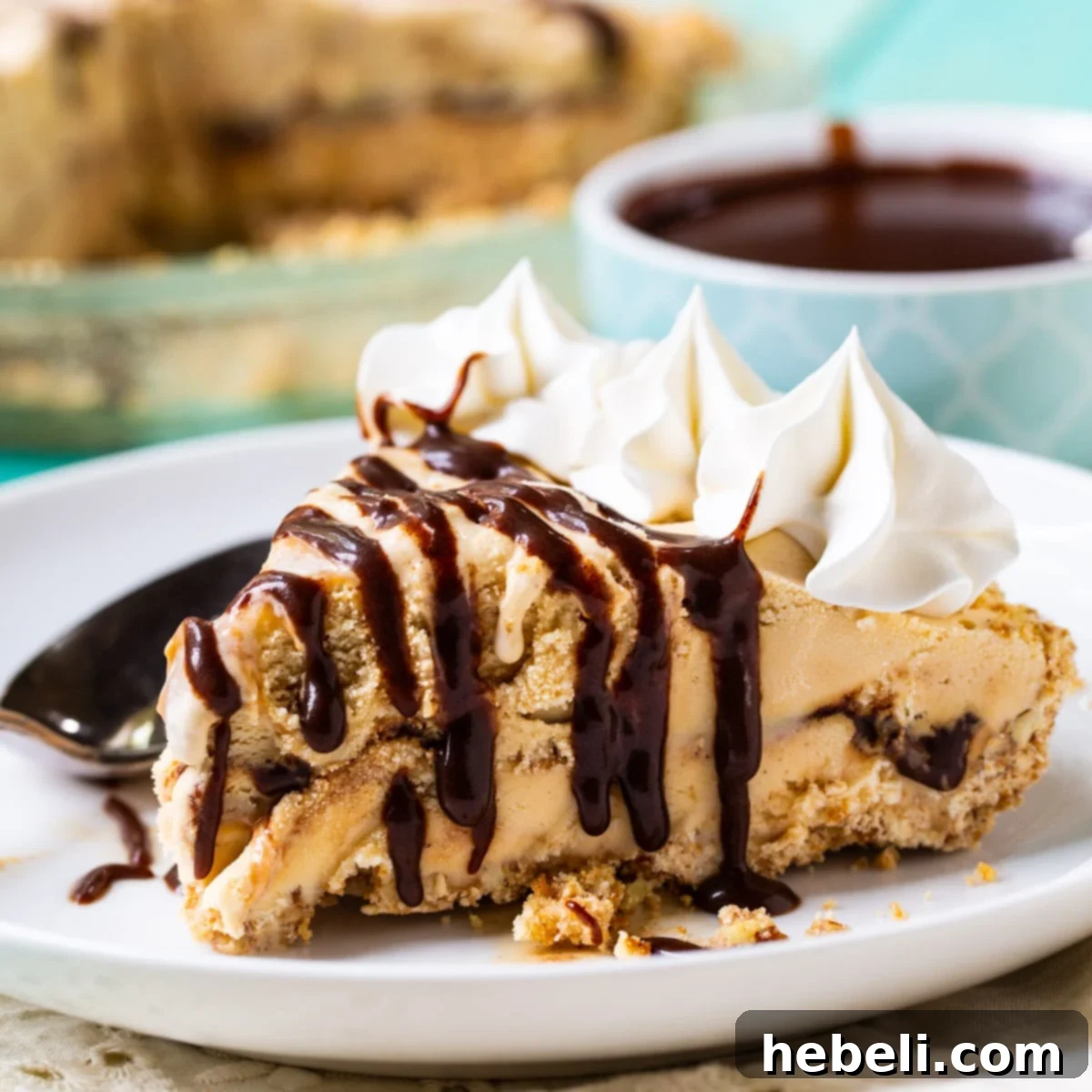 A delectable slice of Dulce de Leche Ice Cream Pie, showing layers of creamy ice cream, crispy crust, and a generous drizzle of mocha fudge sauce, on a white plate with a spoon.