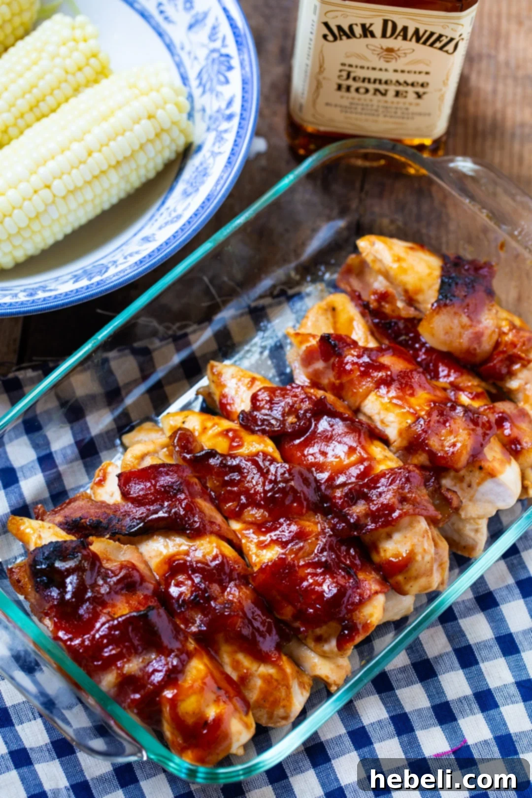 Jack Daniels Glazed Bacon Chicken 3 Cooked Bourbon BBQ Chicken in a 9x13-inch baking dish, accompanied by a bowl of fresh corn and a bottle of Jack Daniels bourbon, highlighting the key ingredients.