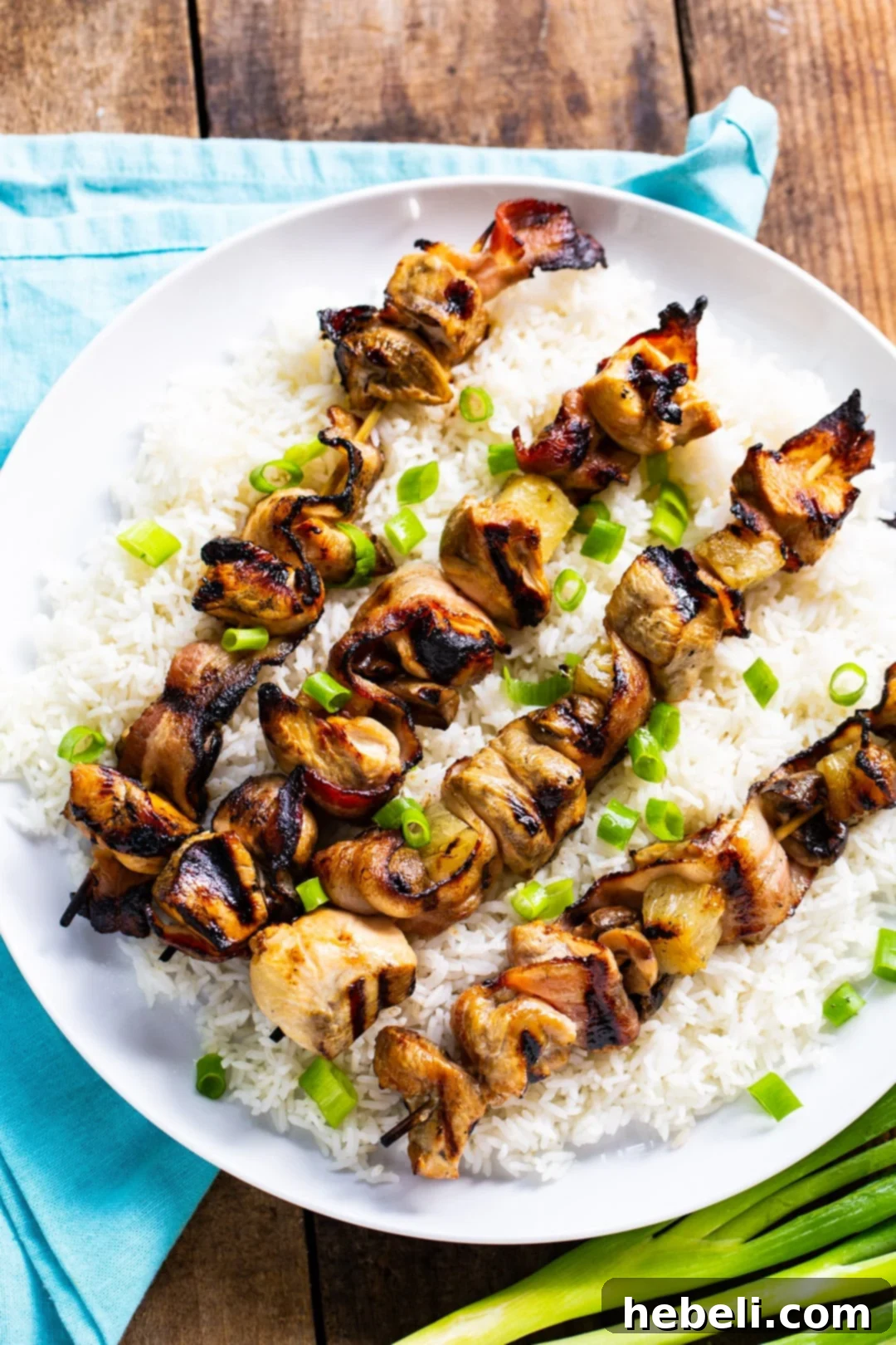 Grilled Chicken and Bacon Skewers 3 Four beautifully arranged Chicken and Bacon Kabobs presented on a serving plate, accompanied by a side of white rice, ready to be enjoyed.