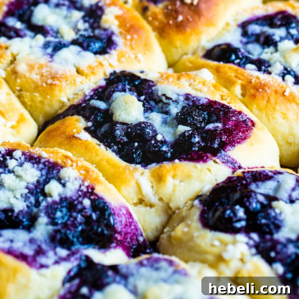 Bursting Blueberry Kolaches 2 Freshly baked Blueberry Kolaches cooling on a baking tray, showcasing their golden crusts and vibrant blueberry centers.