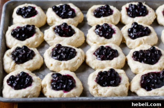 Bursting Blueberry Kolaches 4 Raw kolache dough balls on a baking sheet, with depressions in the center ready for filling.