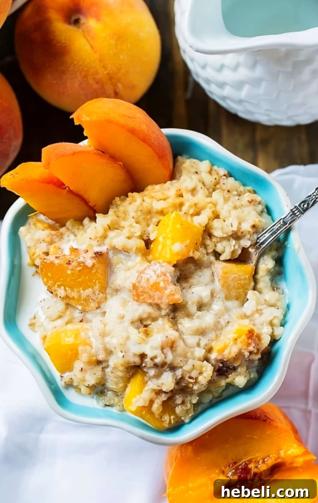 Creamy Slow Cooker Peach Oatmeal 5 A beautifully presented bowl of Crock Pot Peaches and Cream Oatmeal, garnished with fresh peach slices and a cinnamon stick, against a backdrop of whole peaches.