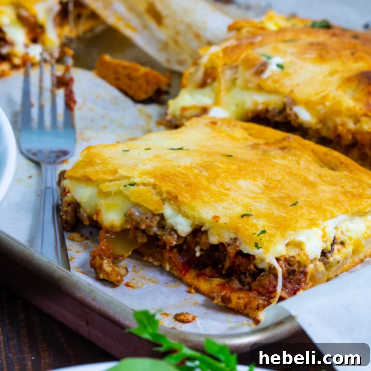 A square of unbaked Crescent Lasagna on a baking sheet, showing the layers of dough, meat, and cheese before baking.