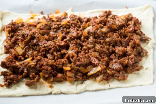 Close-up view of the creamy cheese filling layer generously spread over the savory meat sauce in the Crescent Lasagna before adding the top crust.