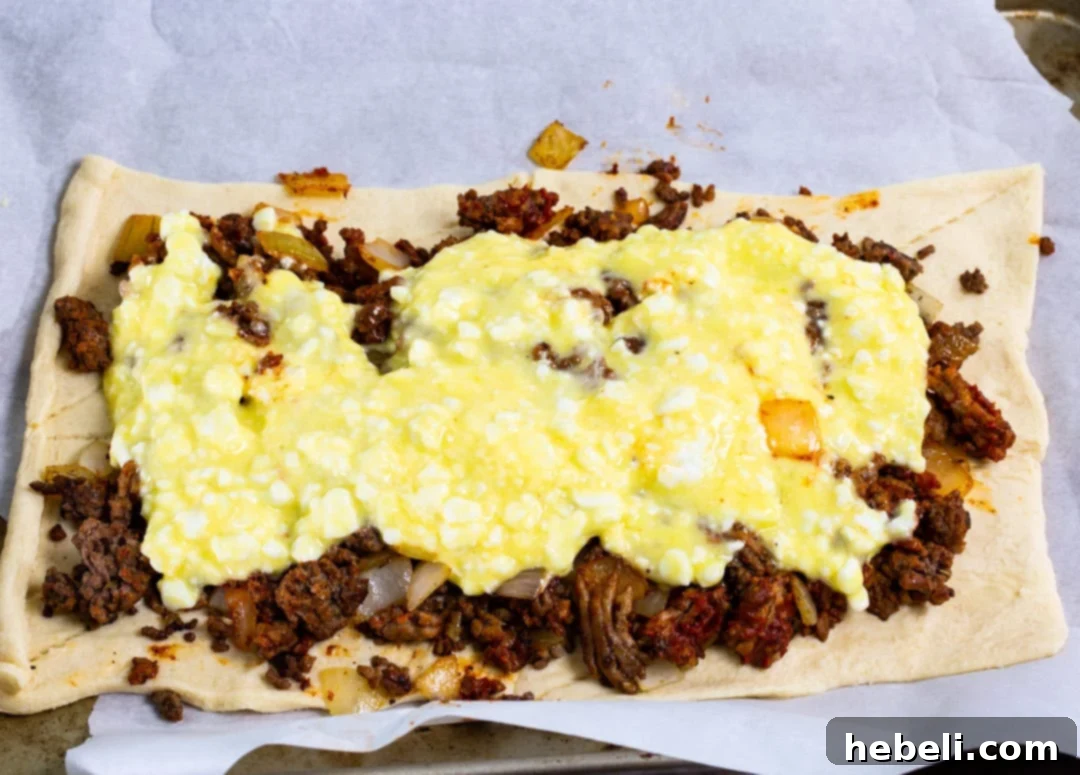 Assembly shot of Crescent Lasagna showing the layered ingredients: bottom crescent dough, meat sauce, cottage cheese, and mozzarella cheese.