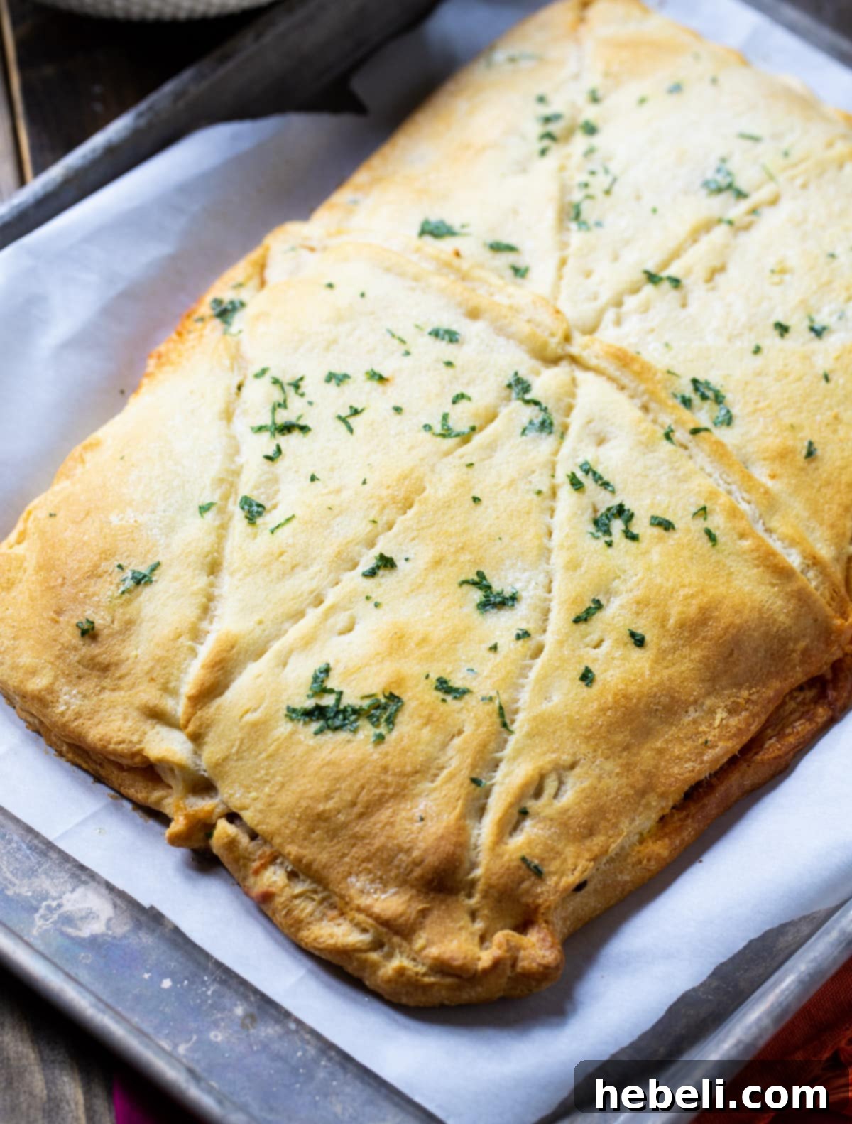 A whole baked Crescent Lasagna, featuring a golden-brown crust and bubbling cheese, presented on a rimmed baking sheet fresh from the oven.