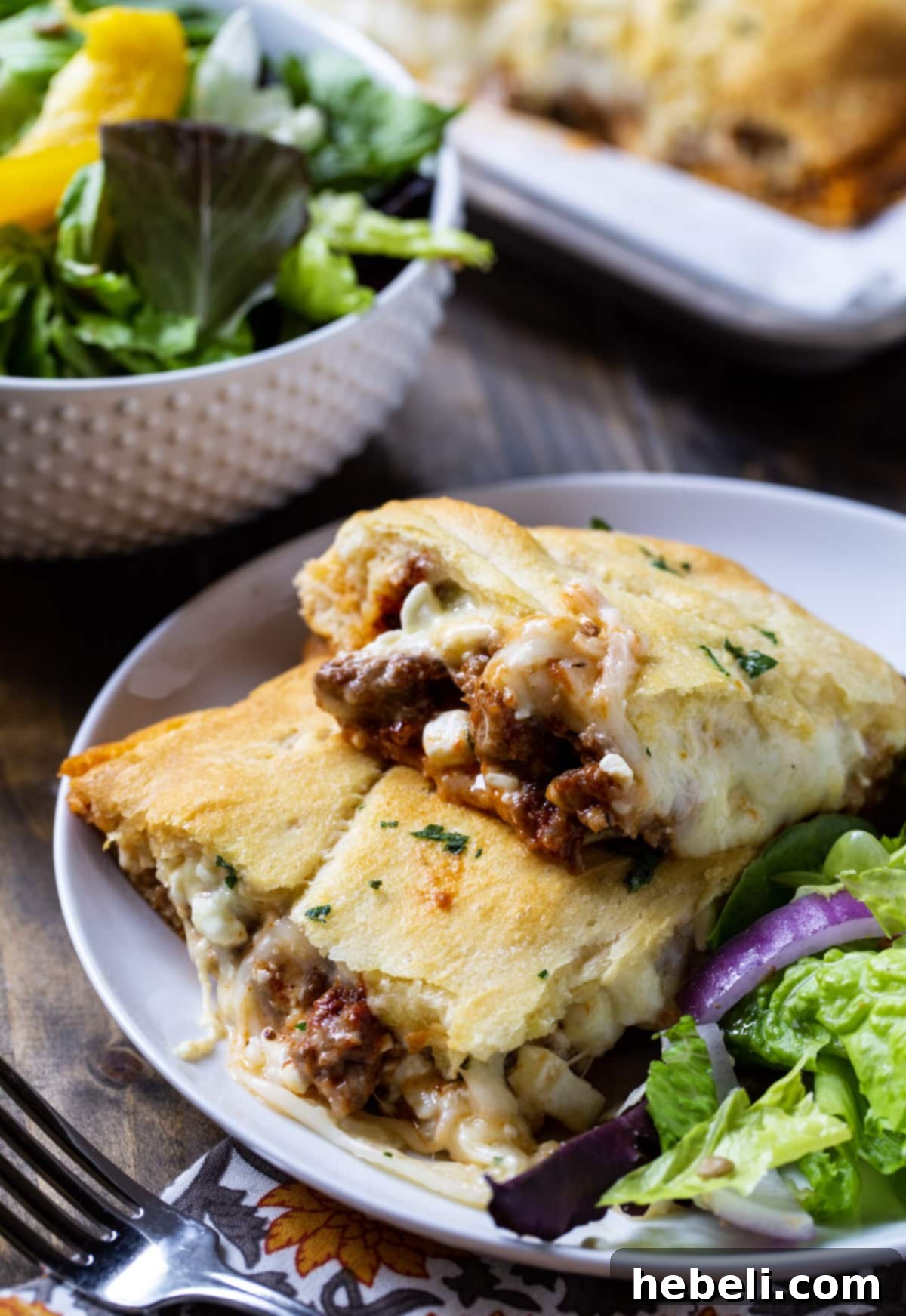 A generous slice of Crescent Lasagna served on a white plate, accompanied by a fresh side salad, highlighting its delicious layers and golden crust.