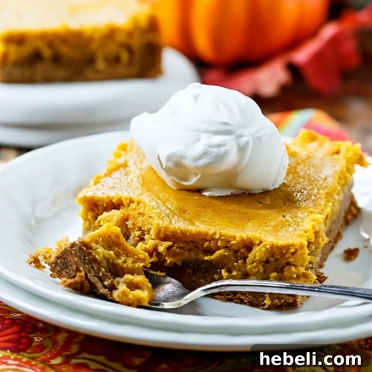A delectable slice of Pumpkin Spice Gooey Butter Cake, generously topped with fluffy whipped cream, inviting you to take a bite.