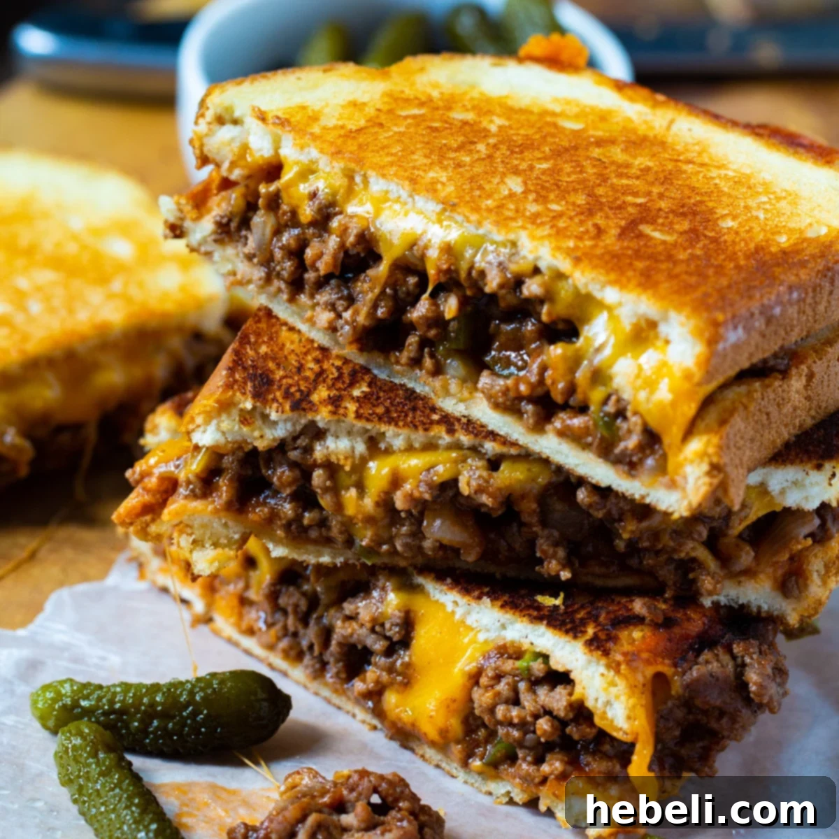 Two halves of a Sloppy Joe Grilled Cheese sandwich, stacked, showing the rich, savory filling and deliciously melted cheddar cheese.