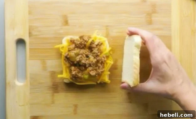 Assembling the Sloppy Joe Grilled Cheese sandwich with shredded cheddar cheese and a spoonful of sloppy joe filling.