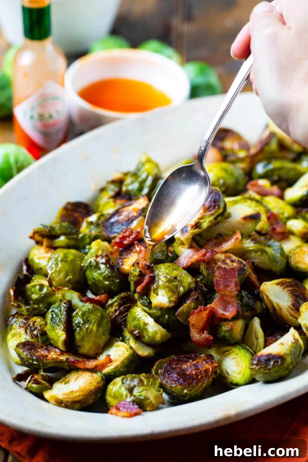 Freshly roasted Brussels Sprouts with bacon being drizzled generously with the homemade Tabasco Honey Glaze.