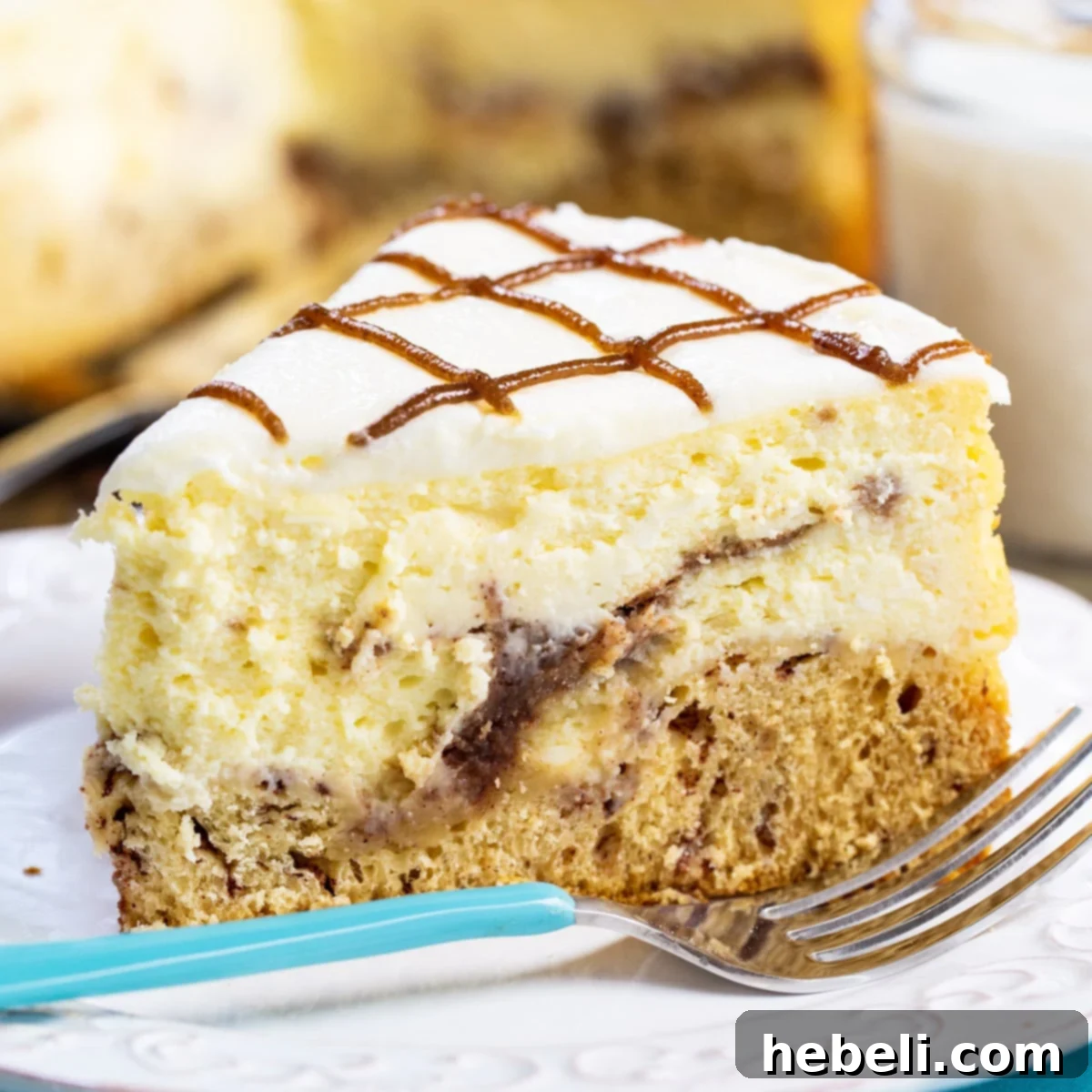 Cinnamon Swirl Cheesecake 2 A perfectly sliced piece of Cinnamon Roll Cheesecake, showcasing its distinct layers of cinnamon roll crust, creamy filling, and luscious glaze, resting on a pristine white plate.