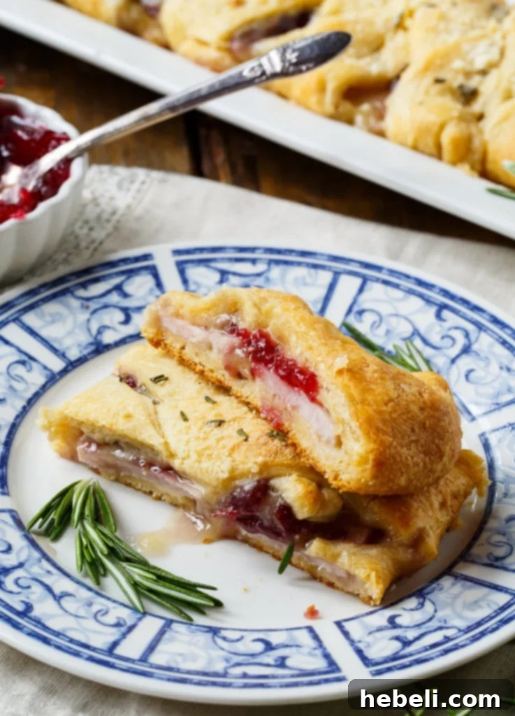 Festive Turkey Cranberry Brie Crescent Braid 7 A beautifully braided Turkey, Cranberry, and Brie Crescent Braid on a cutting board, garnished with fresh rosemary, ready to be sliced and served