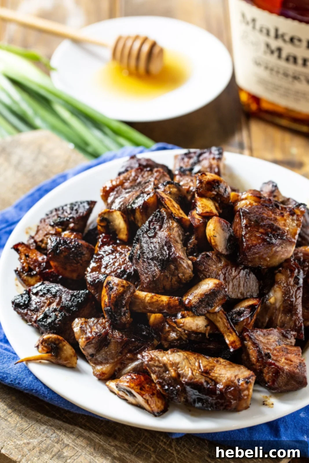 Honey Bourbon Steak Tips with mushrooms on a plate, alongside a bottle of bourbon.