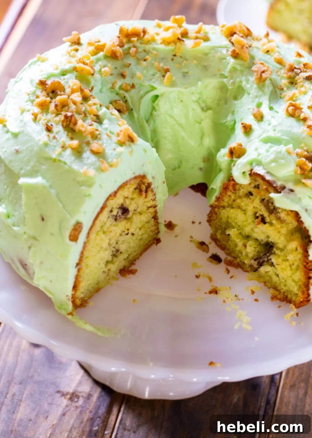 A whole Watergate Cake, freshly baked and frosted, sitting elegantly on a white cake stand against a soft, blurred background, highlighting its inviting texture.