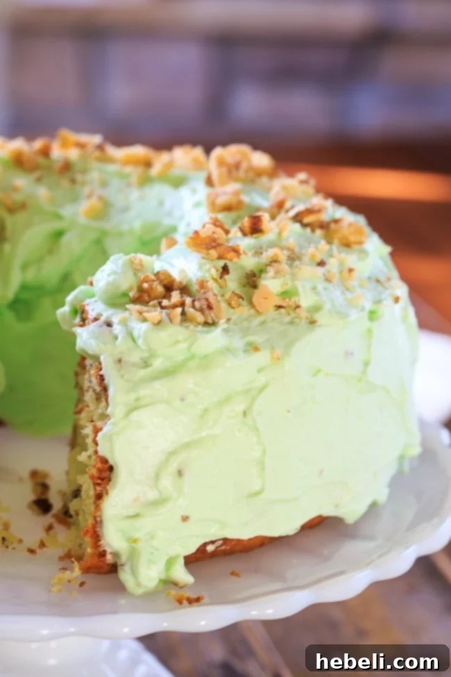 A beautifully presented Watergate Cake, glistening with its rich green frosting and a sprinkle of walnuts, ready to be served and enjoyed by everyone.