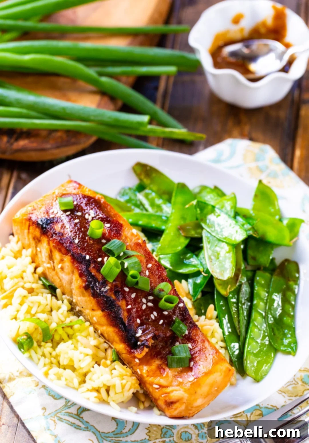 A perfectly cooked Teriyaki Salmon fillet served over a bed of white rice, accompanied by bright green snow peas.