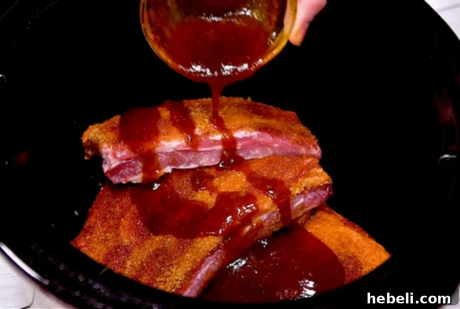 Pouring homemade BBQ sauce over generously seasoned ribs placed inside a slow cooker