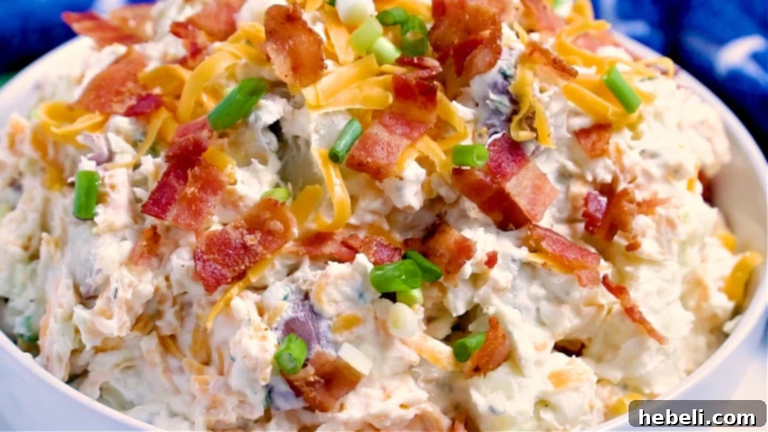 A beautifully composed image of Loaded Ranch Potato Salad in a blue and white patterned serving bowl, garnished with green onions and bacon bits, resting on a rustic wooden surface, highlighting its appetizing appeal.