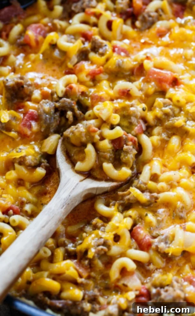 Stovetop mac and cheese stirred with melted shredded cheddar cheese, showcasing the creamy texture.