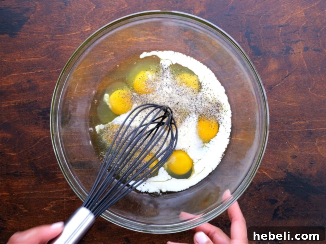 Whisking eggs and milk vigorously in a bowl to create the casserole base.