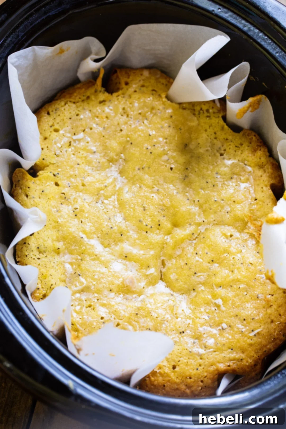 Crock-Pot Lemon Cloud Cake 3 Close-up of the lemon cake baking in a slow cooker, lined with parchment paper, showcasing its golden-brown top.