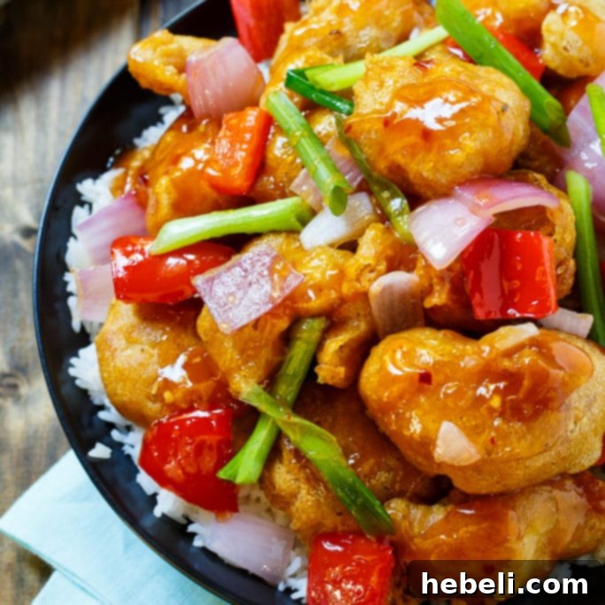 Golden crispy Sweet and Sour Chicken pieces coated in a vibrant sauce, garnished with fresh vegetables.