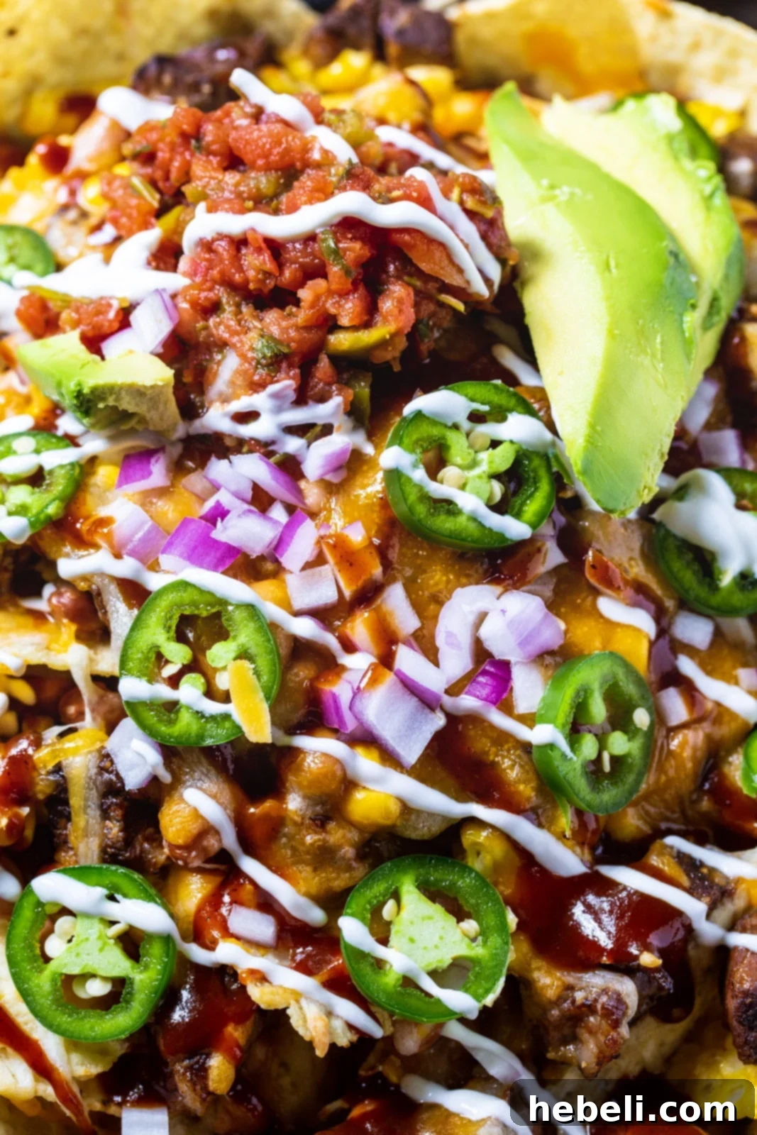 A close-up view of BBQ Steak Nachos generously topped with vibrant sliced jalapenos, showcasing the melted cheese and juicy steak.