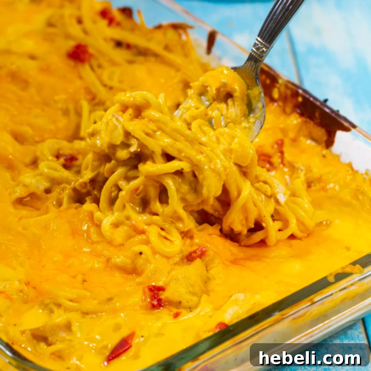 Kickin' Chicken Spaghetti 2 A fork scooping up a generous portion of cheesy Spicy Chicken Spaghetti from a casserole dish, highlighting the creamy texture and melted cheese.