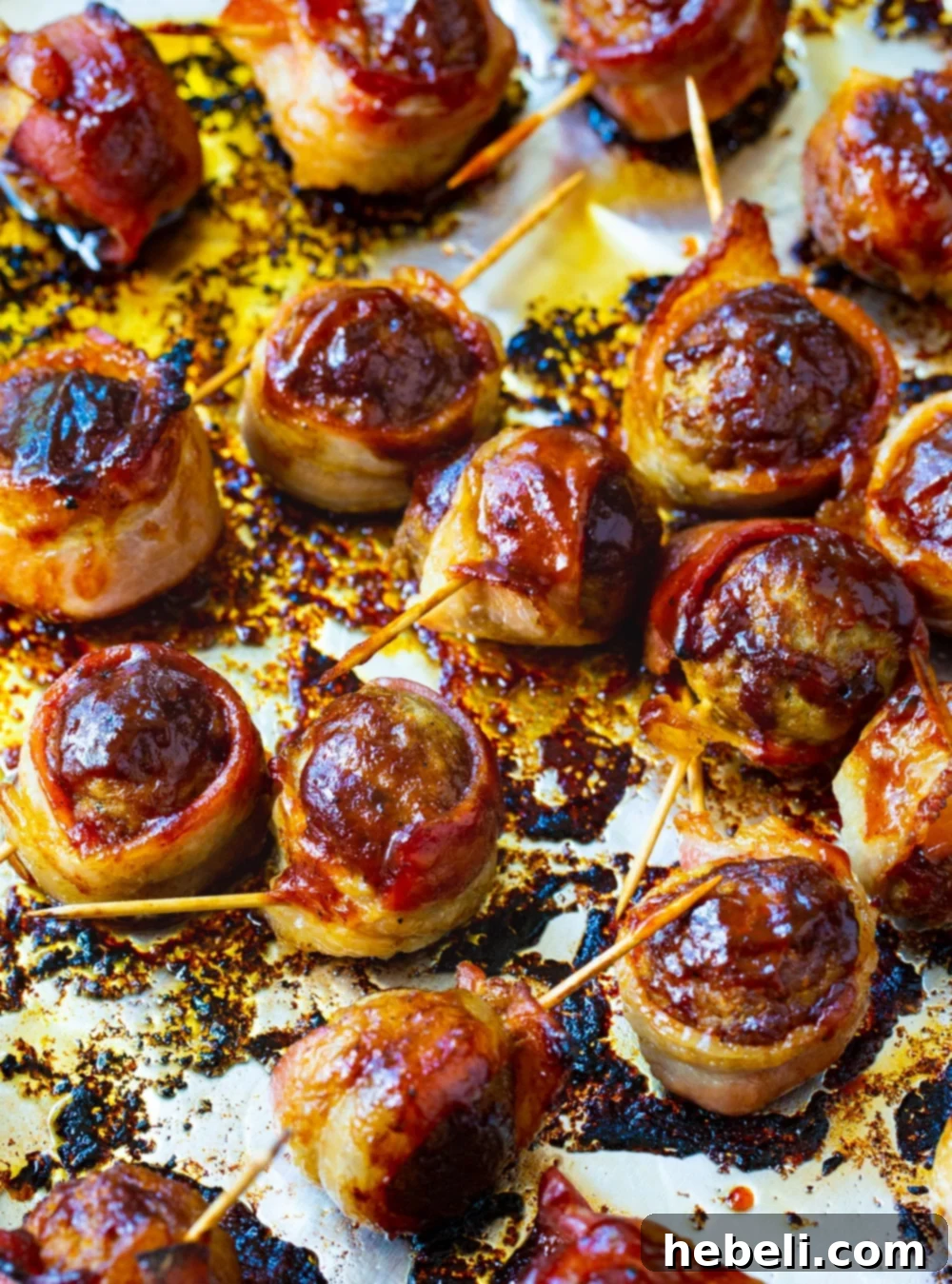 Partially defrosted frozen meatballs, individually wrapped with bacon and secured with toothpicks, arranged on a baking sheet before cooking.