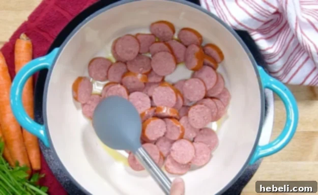 Slices of smoked sausage browning in a Dutch oven with oil.