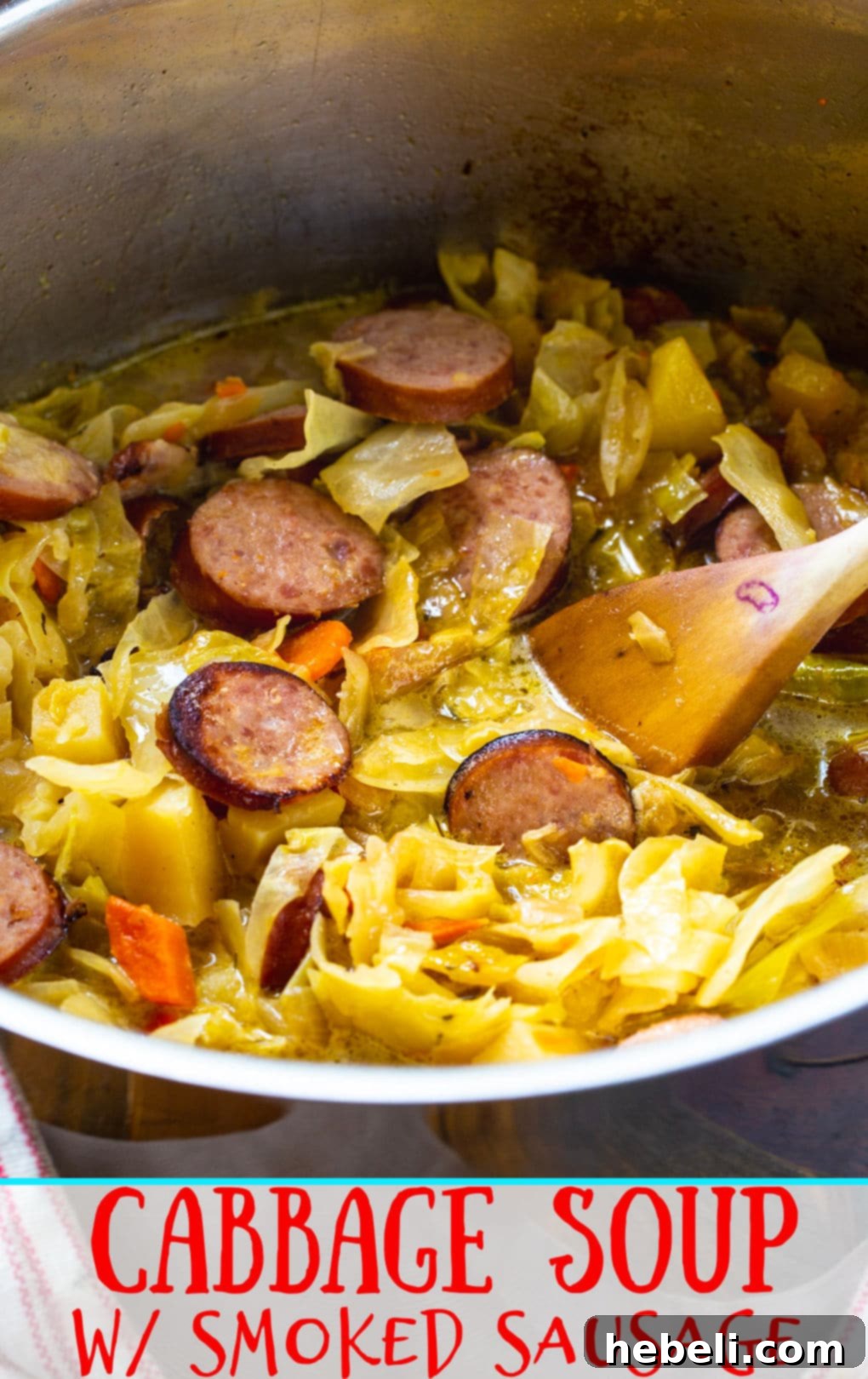 Wooden spoon scooping a generous portion of Cabbage Soup with Smoked Sausage from the pot, ready to serve in a bowl.