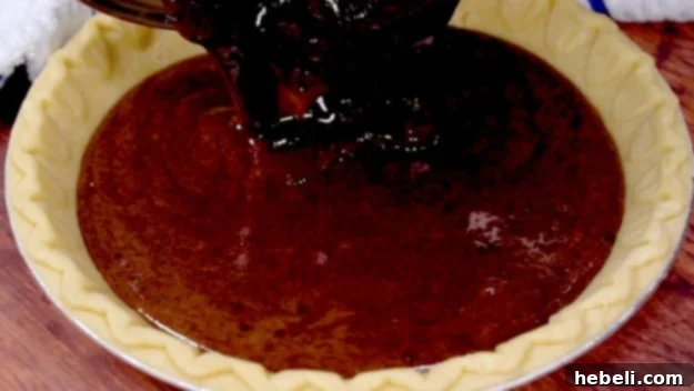 Brownie batter being poured into an unbaked pie crust.