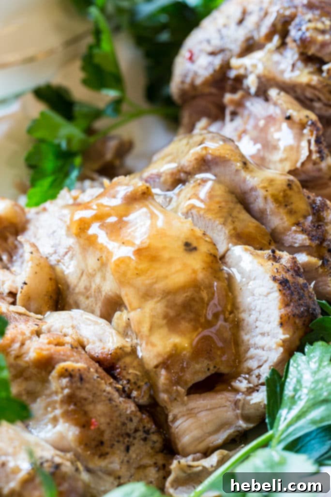 Crock Pot Pork Loin resting with a spoon of gravy, showcasing its tender texture
