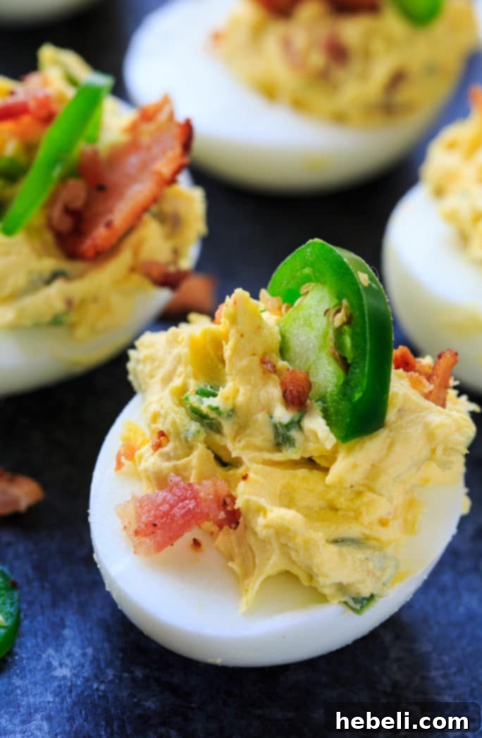 A hand holding a finished Jalapeno Popper Deviled Egg garnished with bacon.