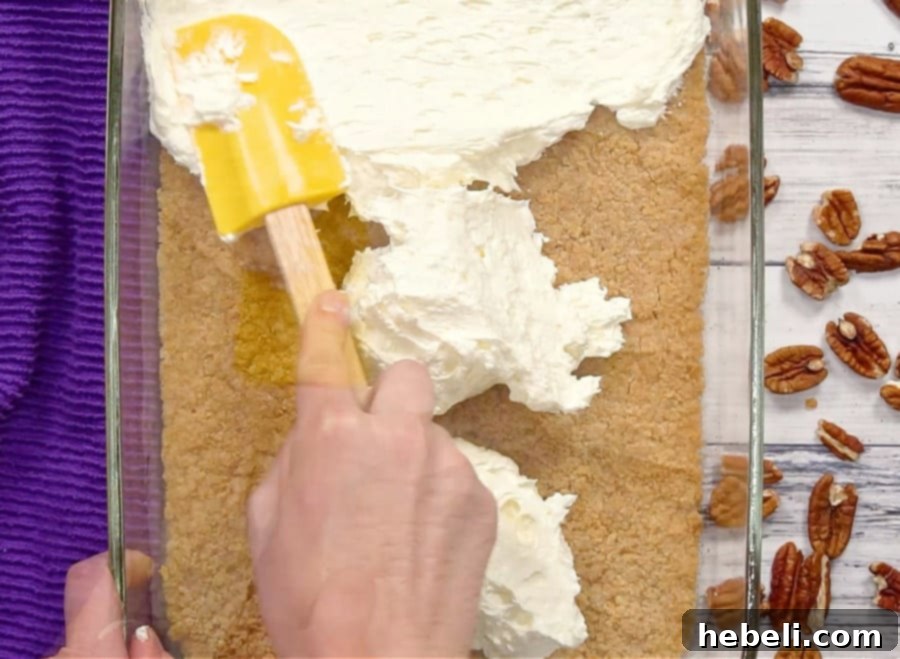 Spreading the smooth and creamy cream cheese layer over the graham cracker crust.