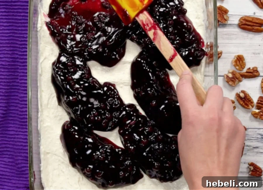 Carefully spreading blueberry pie filling over the creamy cheese layer.