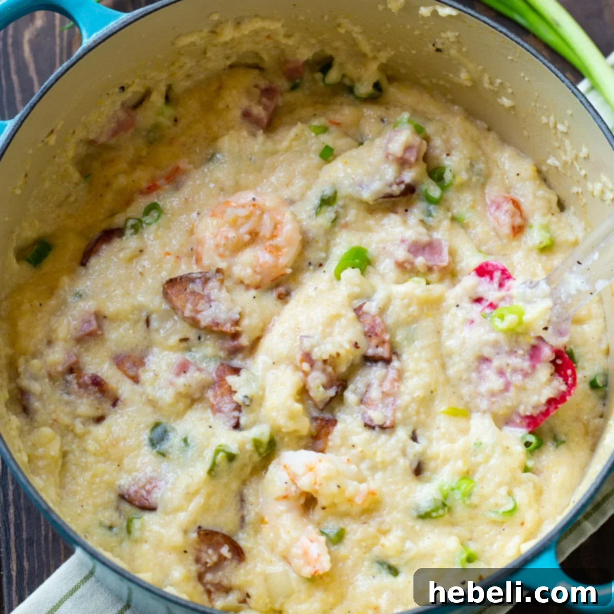 A Dutch oven filled with creamy Jambalaya Grits, garnished with fresh herbs, showcasing shrimp, sausage, and ham.
