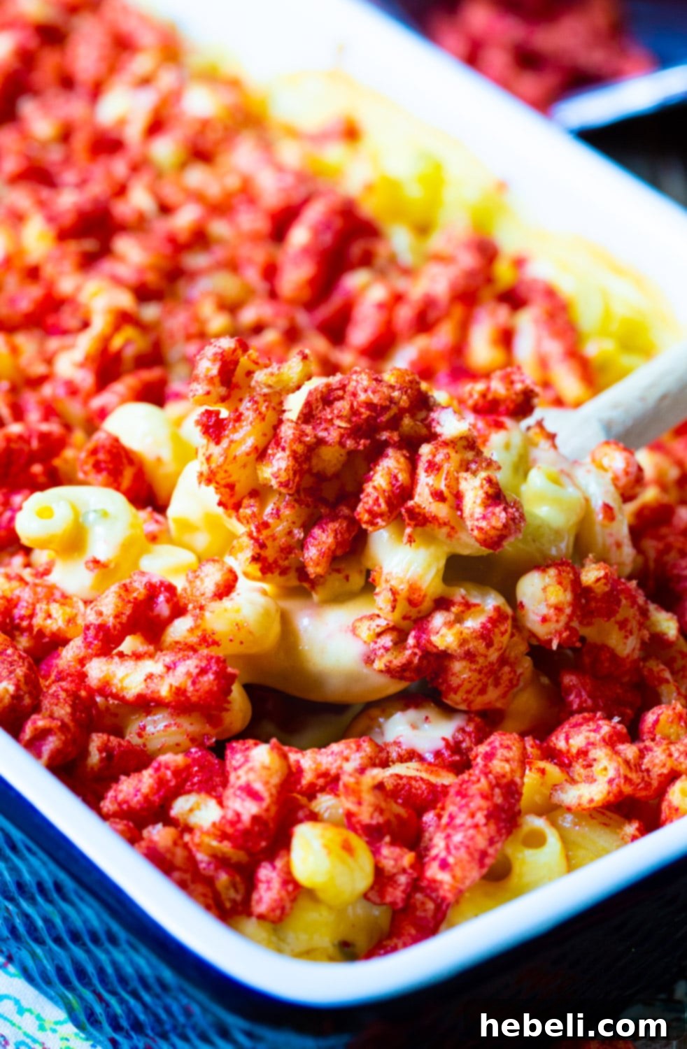 Close-up of a serving of Mac and Cheese with bright red Flamin' Hot Cheetos pieces on top, showcasing the texture.
