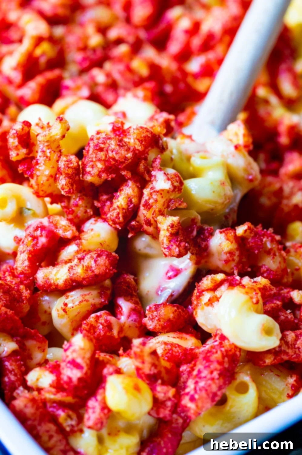 A spoon scooping a generous portion of steaming Flamin' Hot Cheetos Mac and Cheese from a baking dish.