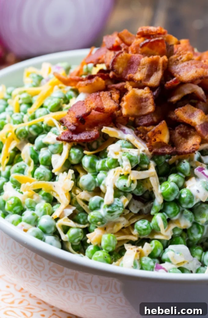 A bowl of creamy pea salad garnished with fresh herbs and more bacon.