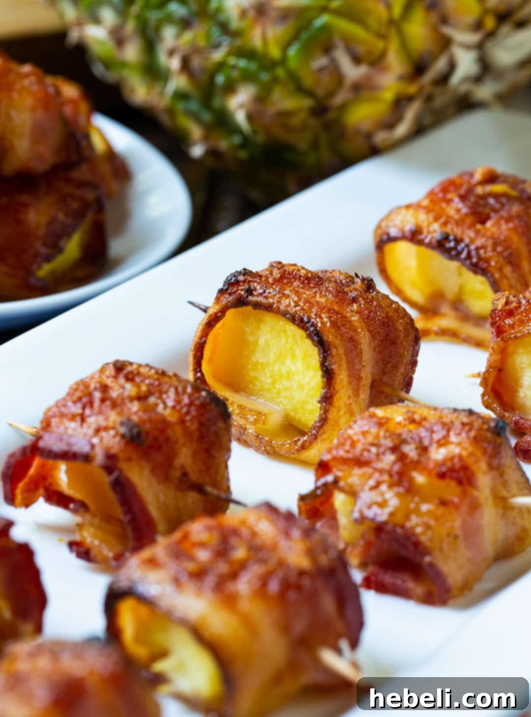 Spicy Bacon Wrapped Pineapple Bites arranged on a decorative serving tray, garnished with fresh herbs.