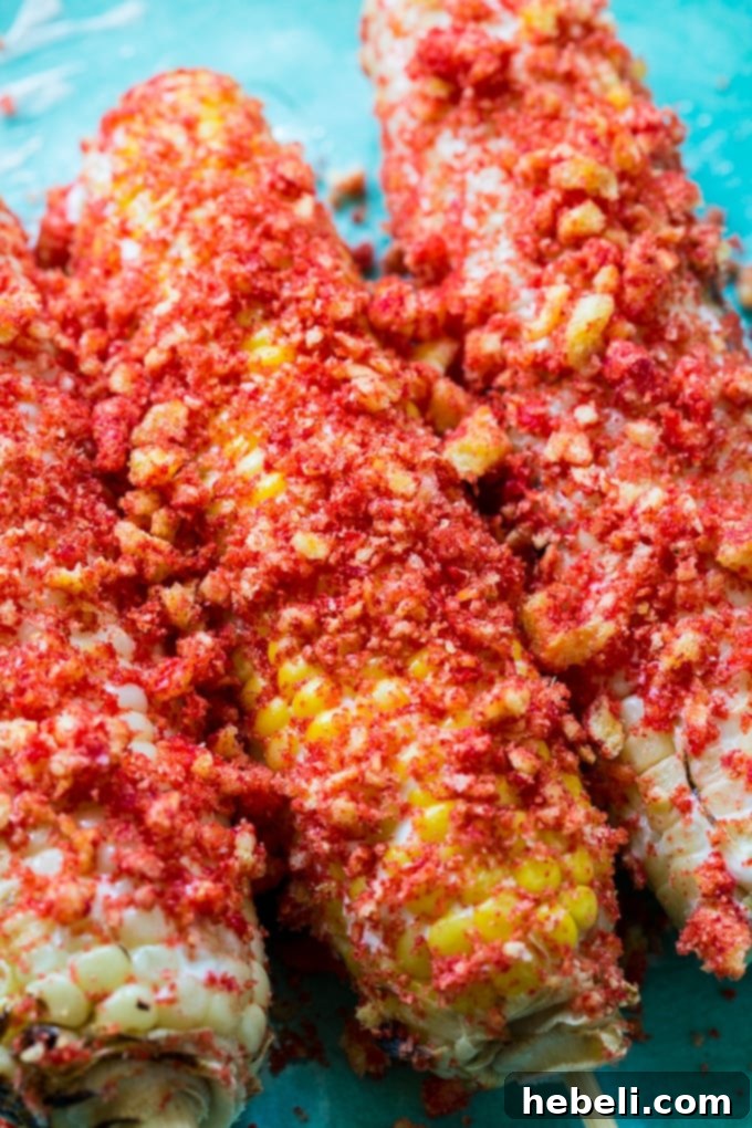 Hands rolling grilled corn in a vibrant pile of crushed Flamin' Hot Cheetos