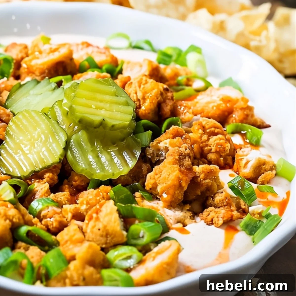 Creamy Nashville Hot Chicken Dip topped with vibrant pickle slices and green onions, served with tortilla chips.